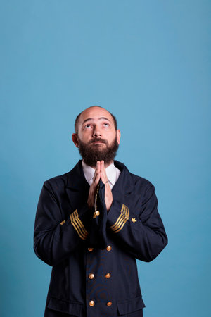 Airline pilot in uniform praying to gods, looking upwards, standing with folded hands gesture....
