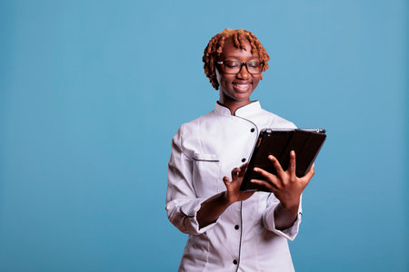 Female chef with digital tablet standing in studio while looking up recipes for new menu items. Head...