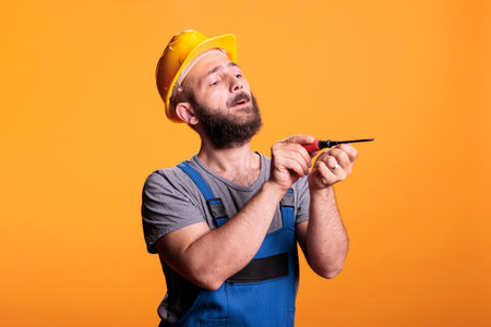 Building craftsman using screwdriver to drill nails, carpenter dressed in overalls with hardhat and...