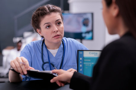 Nurse showing patient expertise to receptionist discussing disease symptoms while asking her to programming another examination. Medical staff working in hospital waiting area, health care supportの写真素材