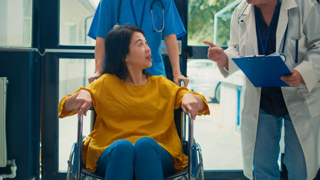 Asian woman with physical disability receiving help from nurse, having checkup visit appointment...