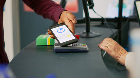 Male client buying vitamins with mobile phone nfc payment, using smartphone at pos terminal in drugstore. Person paying for medicaments and drugs at pharmacy counter. Close up. Handheld shot.の写真素材