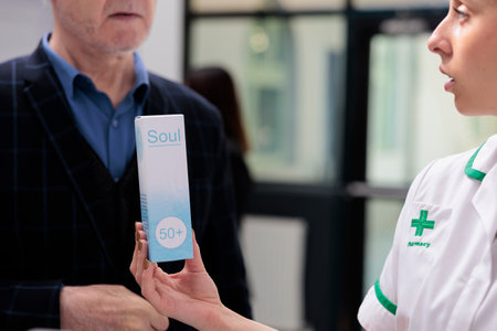 Chemist holding sunblock package, recommending elderly man dermatologic product in pharmacy shop....