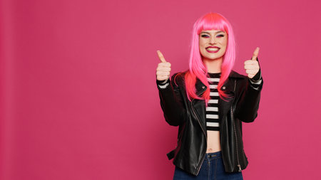 Glamour positive girl showing like and thumbs up symbol on camera, doing good agreement gesture. Cheerful trendy woman showing okay and approval sign, advertising success in studio.の写真素材