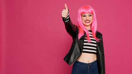 Beautiful trendy model giving thumbs up on camera, advertising like and agreement symbol. Positive carefree woman showing okay and approval gesture, doing success sign in studio.の写真素材