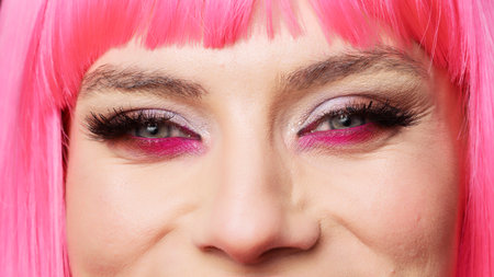 Macro shot of positive woman with glamour colorful eye makeup and pink hair posing in studio, having fun and feeling confident. Healthy positive beauty model with big eyelashes. Extreme closeup.の写真素材