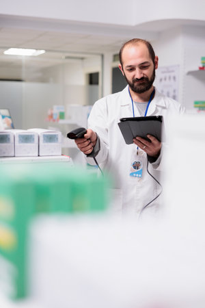 Pharmacist checking medication list on tablet computer while scanning pills packages bar code using...