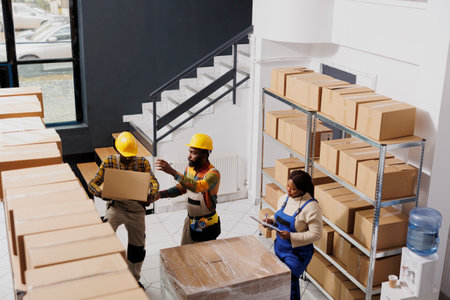 Package handlers team lifting heavy parcel to prepare for transportation. African american warehouse...