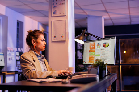 Careful entrepreneur analyzing financial investment graph, typing company profit progress report on computer. Businesswoman working late at night at marketing statistics in startup officeの写真素材