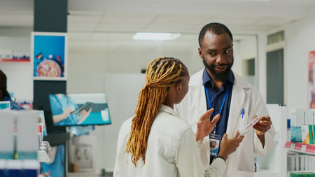 Male doctor giving woman bottle of pills as medicine, recommending pharmaceutics for treatment. Young customer talking to specialist about disease medicaments and vitamins in drugstore.の写真素材