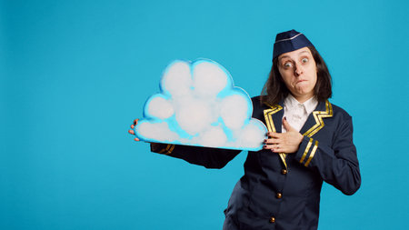 Young stewardess presenting cloud shape billboard, advertising something for aviation industry. Confident air hostess with flying uniform showing isolated cardboard icon, commercial airliner.の写真素材