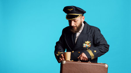 Airline pilot carrying briefcase baggage at job, preparing for commercial flight on camera. Young cabin captain with aviation uniform holding suitcase and working in flying industry.の写真素材