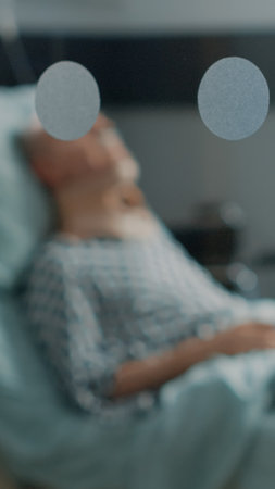 Sick old man laying in hospital ward bed with cervical neck collar at medical facility. Elder patient sitting in intensive care room waiting for surgery diagnosis from doctor to start treatmentの写真素材