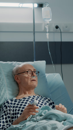 Hospital ward medical surgeon talking to sick patient connected to nasal oxygen tube and IV drip bag. Nurse getting wheelchair to take old man with disease to modern surgery roomの写真素材