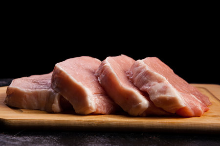 four pieces of fresh raw meat on wooden board on black wooden background. Gourmet food and fresh uncooked mealの写真素材