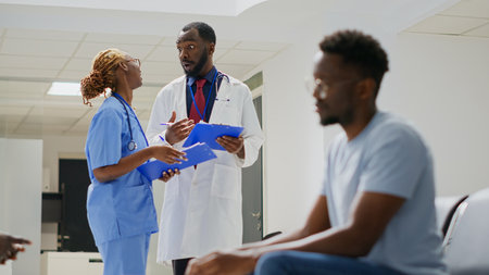 Team of specialists looking at insurance papers in health center lobby, using registration forms and reports to treat patients with disease. Medical workers meeting in waiting room. Handheld shot.の写真素材