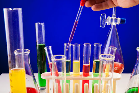 Person hand working in chemistry lab over blue background. Glassware and biology equipmentの写真素材
