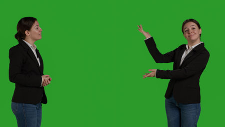 Professional manager pointing aside to show advertisement over greenscreen studio backdrop, creating example ad on blank copyspace. Young adult with suit showing ad icon in front of camera.の写真素材