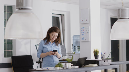 Young entrepreneur using smartphone in startup office, looking at social media website on mobile...