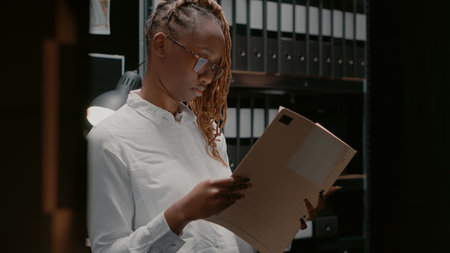 Private investigator analyzing gathered information in police agency office. Woman detective sitting in evidence room and reading archive records, studying clues and case files.の写真素材