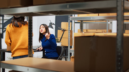 Team of asian workers using laptop to plan shipment, checking quality of goods in warehouse. Depot employees packing products in boxes for order management, financial planning.の写真素材