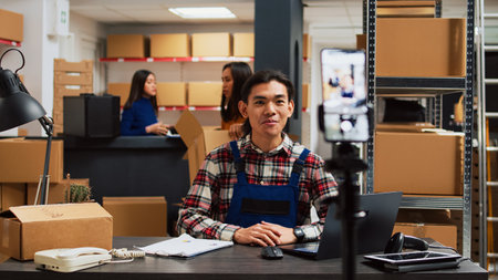 Male employee filming promotion video in warehouse, using social media streaming platform to promote small business in storage room. Young people doing teamwork for advertisement.の写真素材