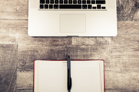 Open writing notebook next to a laptop from above view on a wooden backgroundの写真素材