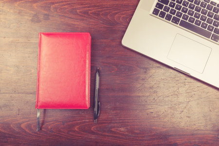 Laptop and a notebook for writing from above view on a wooden backgroundの写真素材