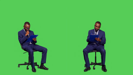 African american businessman taking notes on files, thinking about new corporate ideas over greenscreen backdrop. Male entrepreneur writing business information on papers, sitting on chair.の写真素材