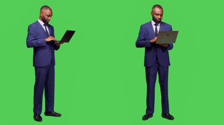Modern employee using laptop to browse network, looking at online website standing over full body greenscreen. Young adult businessman working with wireless computer in studio.の写真素材