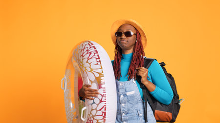 Excited woman carrying inflatable ring, wearing sunglasses and hat before arriving on the beach....