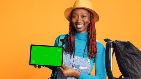 Joyful person holding tablet on camera, working with blank greenscreen template on display. Young adult showing digital device with isolated chroma key template, copyspace on screen.の写真素材