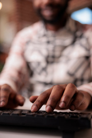 Closeup of african american coder writing software using computer keyboard while working remote from home living room. Selective focus on man freelancer hands typing text while programming.の写真素材