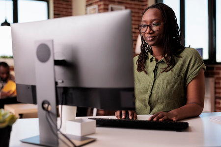 Confident african american freelancer looking at computer screen and typing while working remote...
