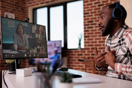 African american man with wireless headphones in online interview with startup owner and human resources team. Team brainstorming business ideas in video call conference working remote from home.の写真素材