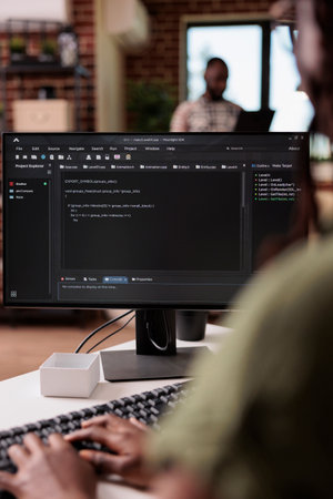 Selective focus on programmer typing code on computer keyboard while roommate is relaxing using...