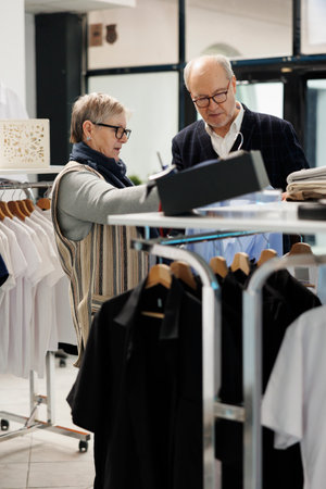 Elderly couple looking at blue stylish shirt analyzing fabric in clothing store, looking at new fashion collection. Caucasian people shopping for formal wear, buying fashionable merchandiseの写真素材