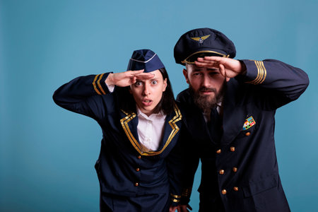 Portrait of airplane capitan and flight attendant couple looking at camera, medium shot. Aircrew team wearing flight uniform while standing in studio with blue backgroundの写真素材