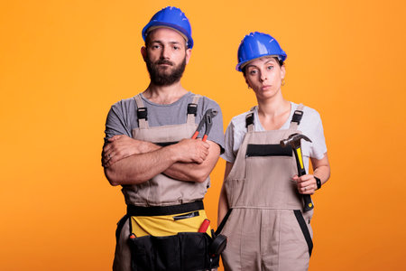 Team of building engineers holding renovating tools on camera, using sledgehammer and pair of pliers to work on renovation project. Builders posing with hammer and pliers over background.の写真素材