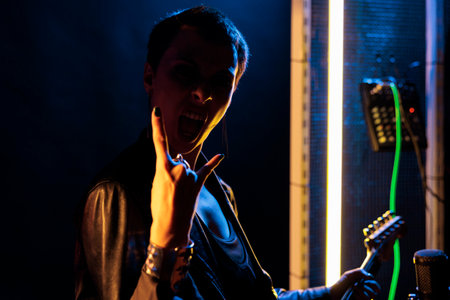 Rebel rockstar woman playing at electric guitar in studio preparing music for rock concert, testing instrument sound. Guitarist performer with grunge jacket performing metal song working at punk albumの写真素材