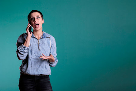 Confident attractive woman using mobile phone to have remote conversation with friend standing over isolated background in studio. Cheerful woman smiling while having smartphone call discussionの写真素材