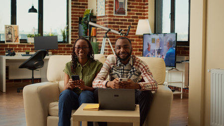 Happy modern couple using smartphones together sitting on couch, browsing internet and social media...