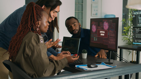 Multiethnic group of it engineers dealing with hacking alert, displaying security server error on computer. Software developers having computer and system hacked, working on database.の写真素材