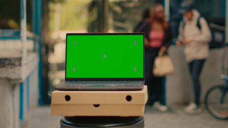 Laptop advertising greenscreen template outside, food delivery service at front door. Running isolated chroma key display with blank mockup and copyspace background on computer screen.の写真素材