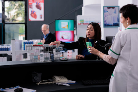 Pharmacy buyer giving cashier medications for scanning at drugstore counter desk. Pharmaceutical employee standing at checkout and using scanner on vitamin packages barcodeの写真素材