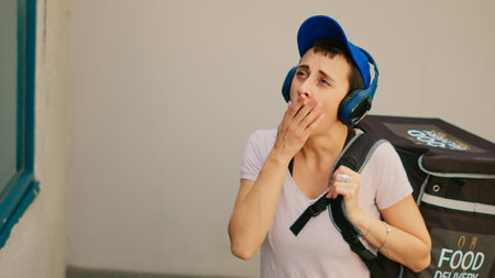 Tired food delivery employee yawning and ringing front door bell to deliver takeaway meal order from...