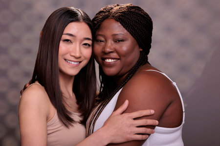 Two diverse women hugging demonstrating confidence, love and self care. Beautiful african american and asian young girlfriends smiling, embracing together and looking at cameraの写真素材