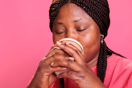 Portrait of joyful friendly model holding cup of coffee drinking hot beverage while posing in studio...
