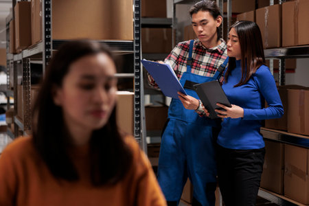 Retail storehouse workers picking customer order using checklist on clipboard. Industrial warehouse employees standing near parcels shelf, analyzing goods list and doing inventoryの写真素材