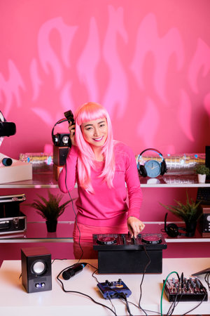 Dj performer with pink hair mixing techno music with eletronic having fun in club during night time, performing song using professional mixer console. Artist celebrating album with fans in studioの写真素材